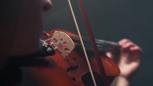 Woman musician lowers the violin and bow, standing in a smoky darkness studio, close-up.