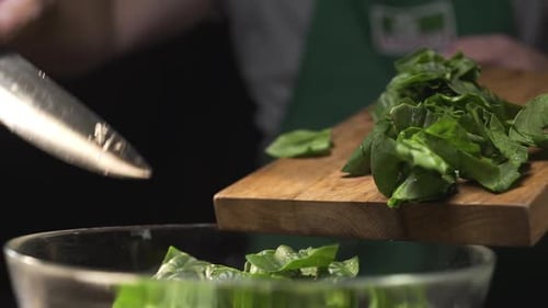 Le cuisinier verse les épinards hachés de la planche à découper dans le bol en verre
