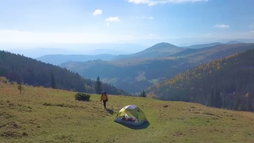 Hiker Approaching Tent in Mountain Landscape