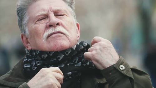 Senior Man Adjusts Scarf in Urban Setting
