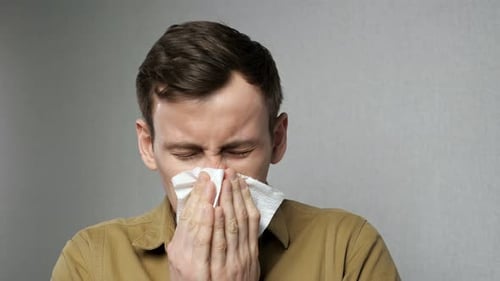 Young Man Sneezing and Wiping Nose with Tissue