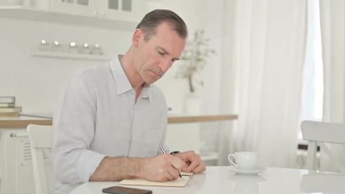 Focused Middle Aged Man Writing in Notebook at Home