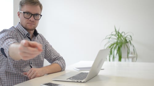 Man Points at Camera While Working on Laptop