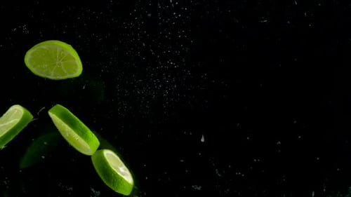 Sliced Limes Falling into Water on Black Background