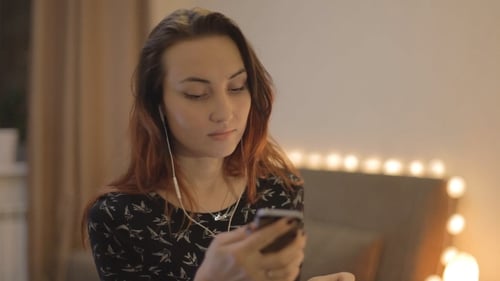 Woman Using Mobile Phone with Headphones On Indoors