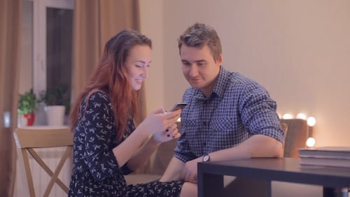Young Couple Looks at a Smartphone Indoors Together