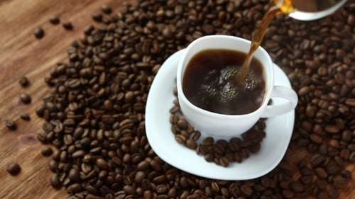 Coffee Pouring Into Cup Surrounded by Coffee Beans