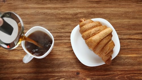 Pouring Coffee Near Golden Croissant on Wooden Table