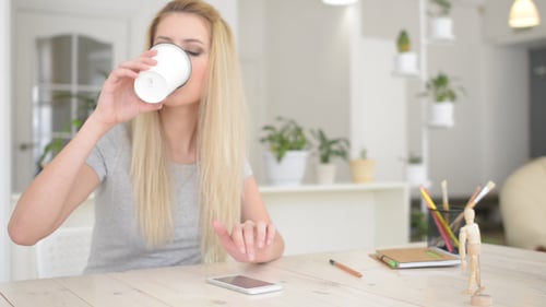 Young Woman Using Cellphone and Drinking Coffee