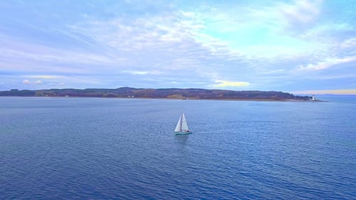 Sailboat Cruising on Water near Coast at Sunset