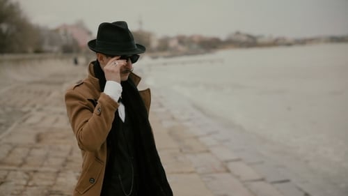 Man in Hat and Coat Poses near Water