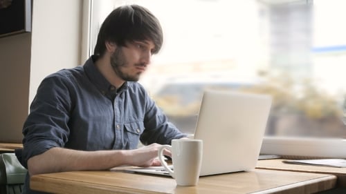 Joyeux jeune pigiste avec ordinateur portable au café