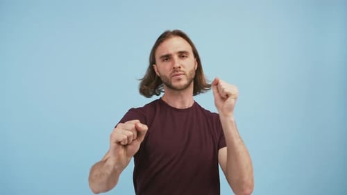 Young Goodlooking Man in Brown Tshirt is Dancing and Smiling While Posing Against Blue Studio