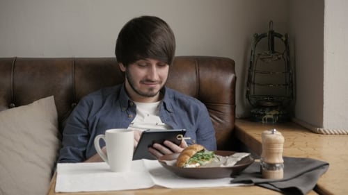 Young Adult Using Tablet While Having Breakfast