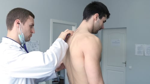 Doctor Examining Young Man with Stethoscope in Clinic