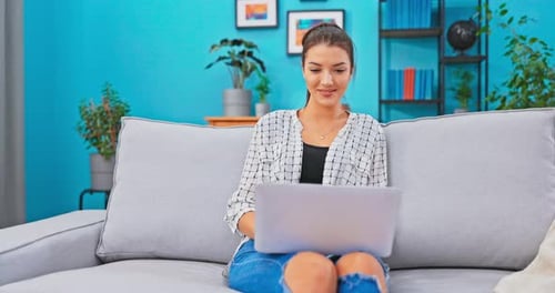 The Young Buisesswoman Works Remotely From Home in Living Room on the Couch Holding Laptop