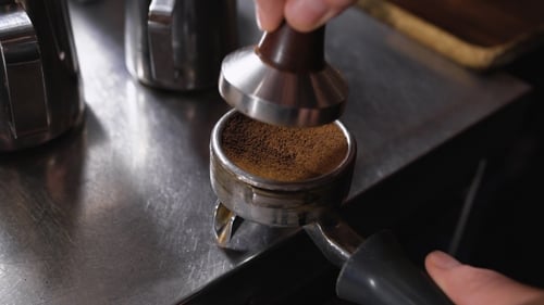Barista Using a Tamper To Press Ground Coffee Into a Portafilter In Cafe On Table