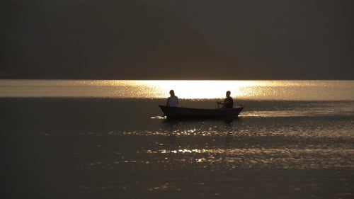 Figures Rowing Boat at Sunrise on Calm Lake