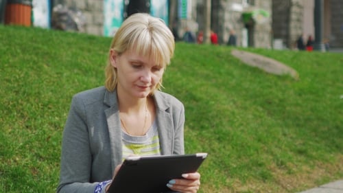 Blonde Woman Enjoys The Tablet In The Park