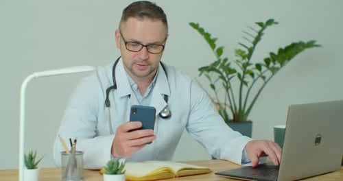Doctor Using Laptop and Mobile Phone at Desk