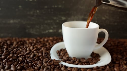 Pouring Black Coffee into Cup Surrounded by Beans