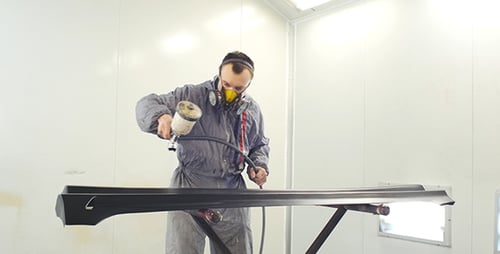 Man Spray-Painting Car Part in Brightly Lit Factory