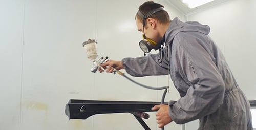 Man Spray Painting Car Part in White Room