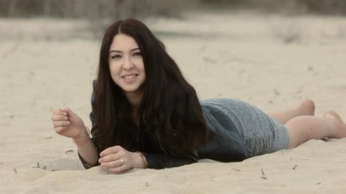 Smiling woman lies on sand in jacket
