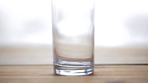 Water Being Poured into Glass on Wood Surface