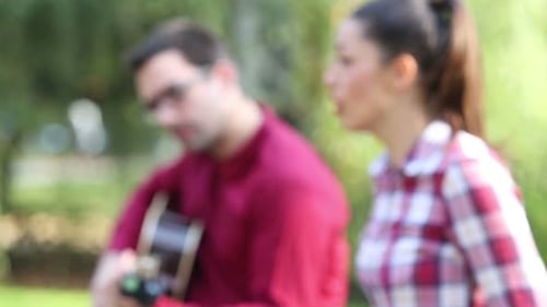 Junges Paar spielt Gitarre und singt im Park 2