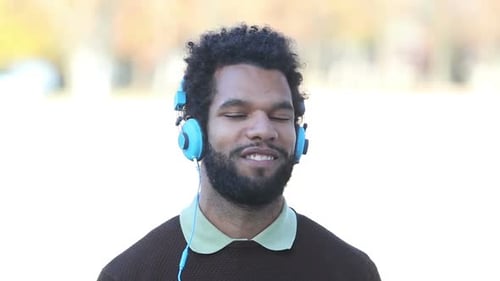 Young Man Puts on Blue Headphones and Smiles