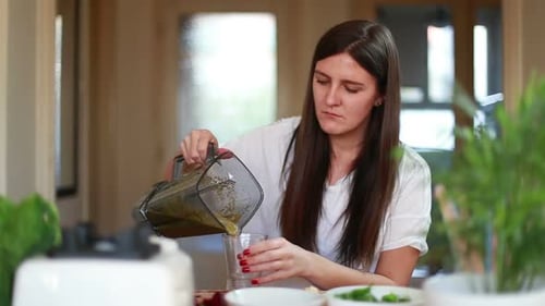 Woman Pouring Green Smoothie Into Glass