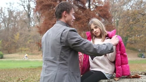 Vater hilft Tochter beim Anziehen von Jacke und Schal im Park