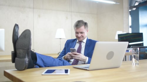 Man in Suit Using Phone With Feet Up