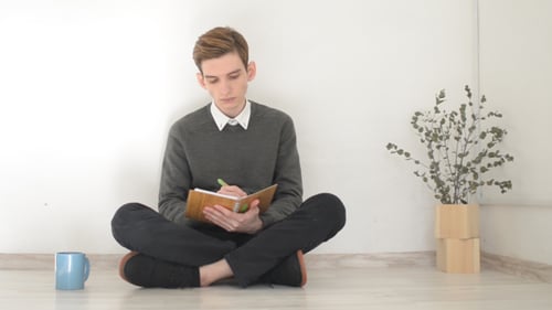 Young Adult Sits Writing in Notebook on Floor