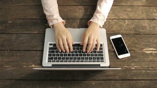 Woman Typing On Laptop Keyboard With Cellphone