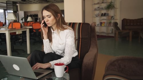 Woman on Cell Phone Using Laptop in Office