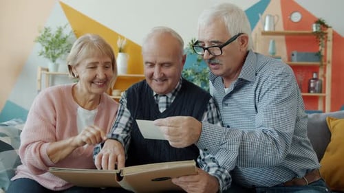 Cámara lenta de hombres y mujeres mayores viendo imágenes en un álbum de fotos hablando en casa