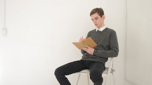 Young Man Writing in Notebook with Green Pen