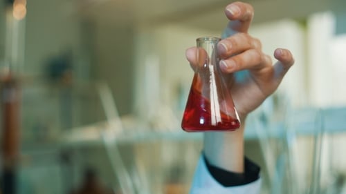 Hand holds red liquid in small laboratory flask