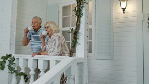 Senior Couple Enjoys Coffee on White Cottage Porch