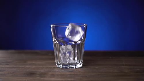 Ice Cubes Falls Into Glass. Slow Motion Transparent Ice Cubes Fall in Glass That Stands on Dark