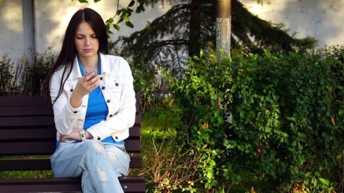 Young Girl Uses The App On Your Smartphone In Park