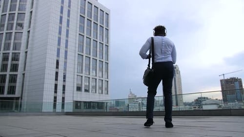 Man Walks Near City Buildings on Rooftop