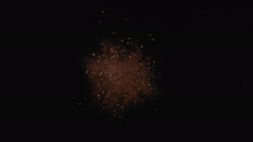 Kaffeebohnen fliegen, nachdem sie vor schwarzem Hintergrund explodiert sind. Zeitlupe.