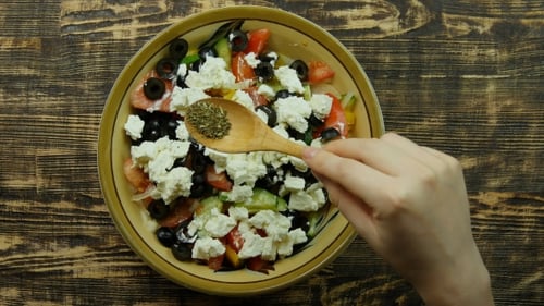 Female Hand Sprinkle Seasoning to Greek Salad