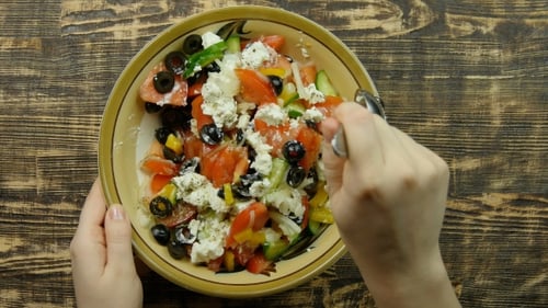 Weibliche Hand rührt frischen Gemüsesalat