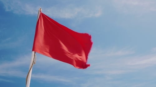 Red Warning Flag Waving Against Blue Sky
