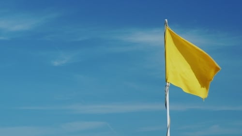 Yellow Flag Waving Against a Clear Blue Sky