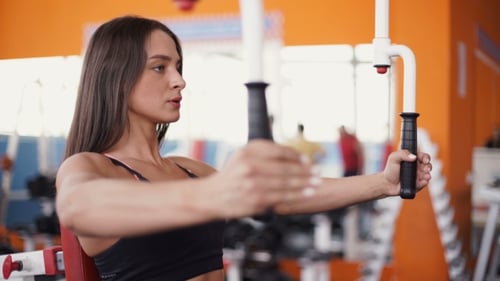 Young Woman Flexing Muscles On Cable Gym Machine.